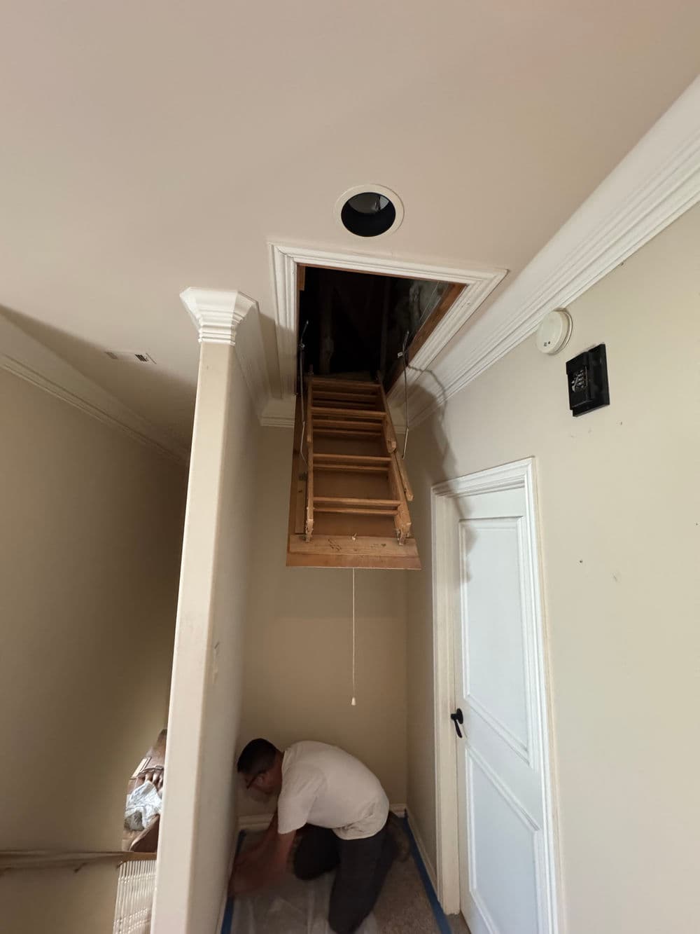 Person installing stairs to an attic with a ceiling opening and wooden ladder.