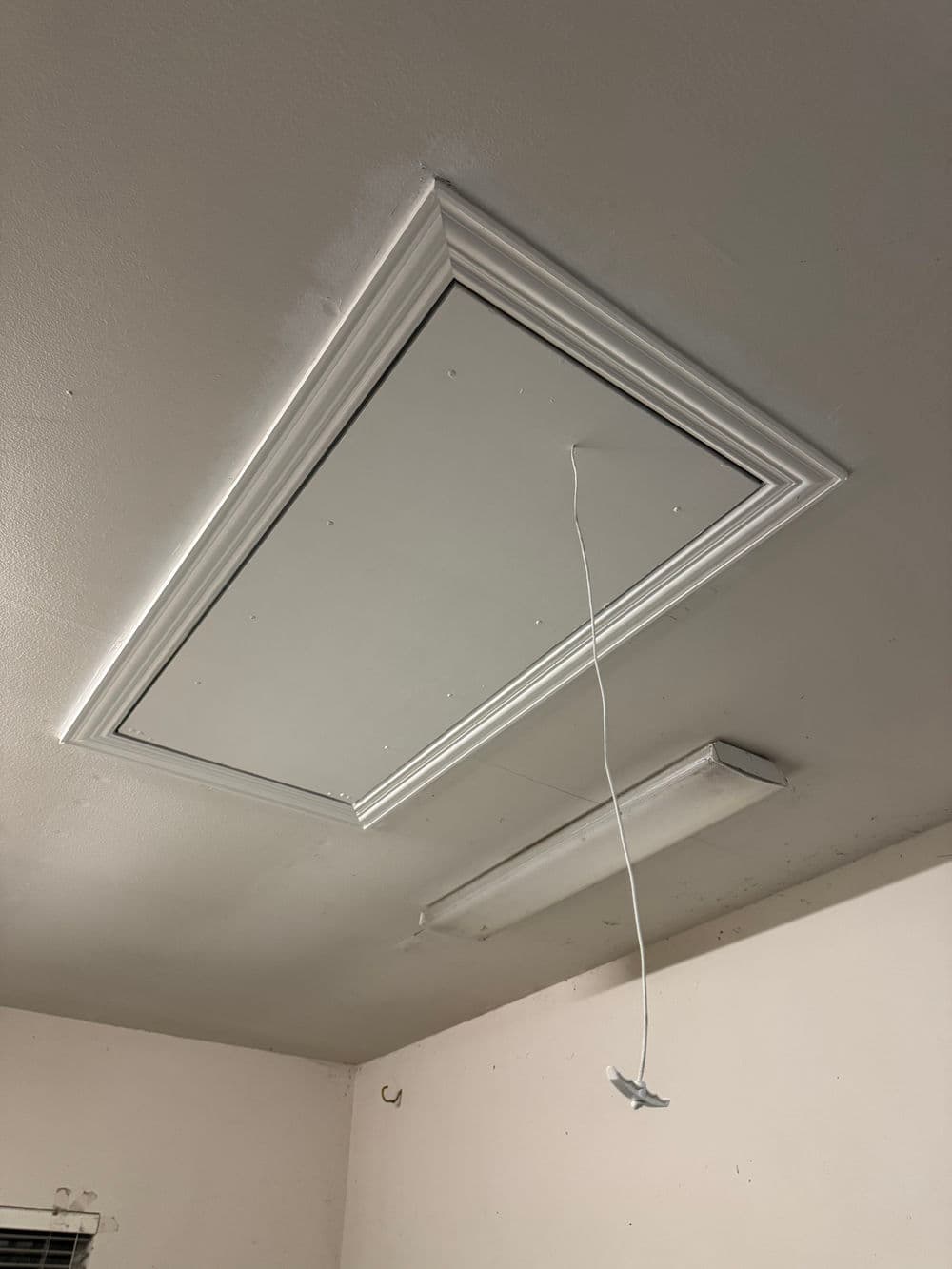 Ceiling access panel with a dangling cord in a light-colored room.